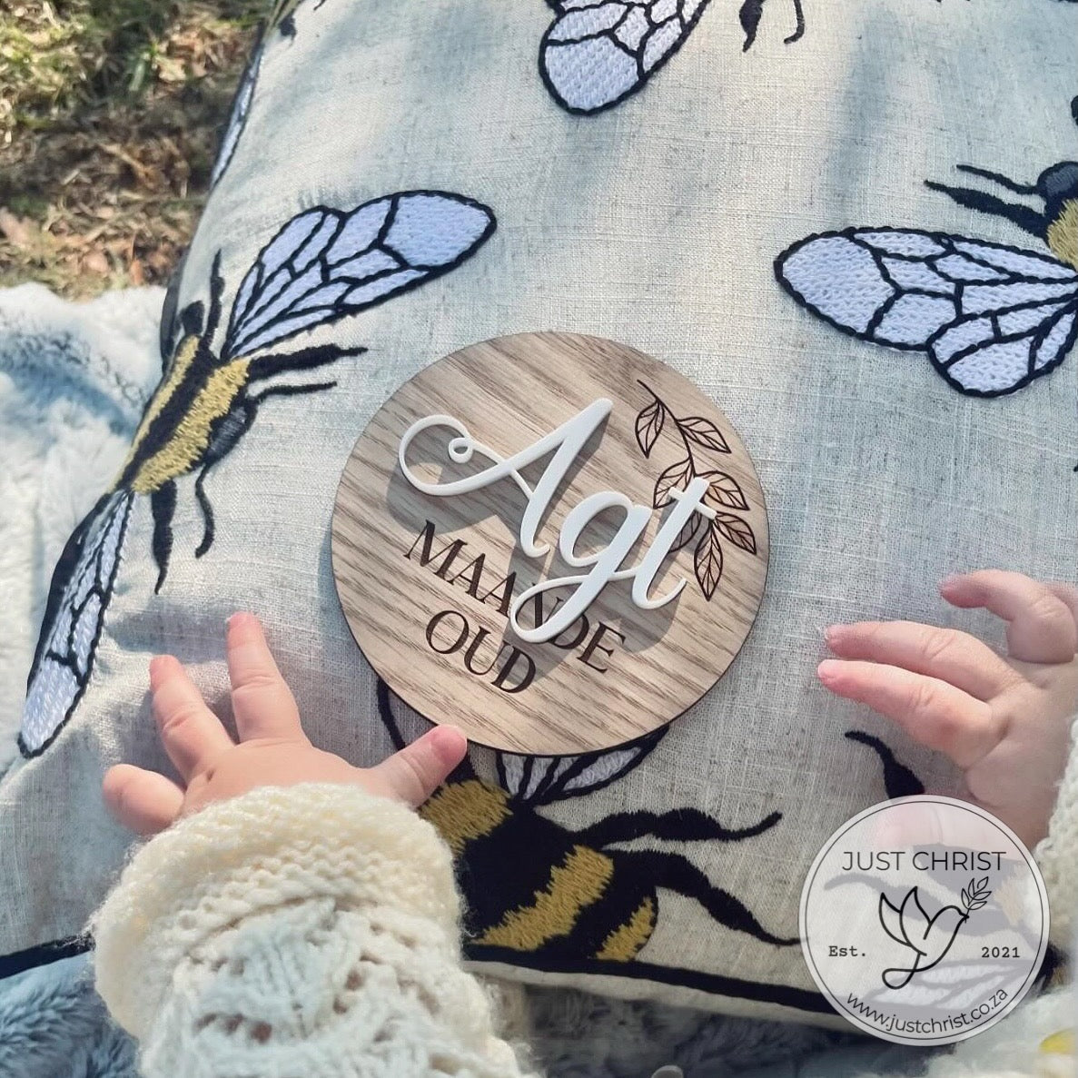 A close up of wooden plaques, each wooden plaque is a monthly milestone disc used for tracking baby's age with a photo album. The wooden plaque is engraved and boasts white acrylic, for example - One (acrylic) month old (engraved). 